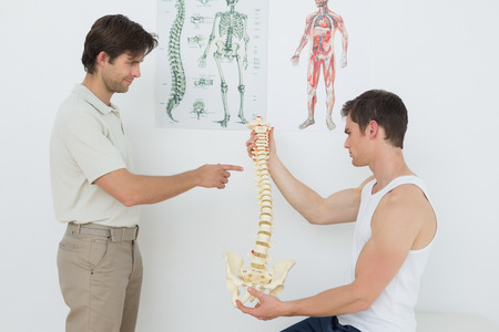 Male physiotherapist showing patient something on skeleton model in medical officeの写真素材