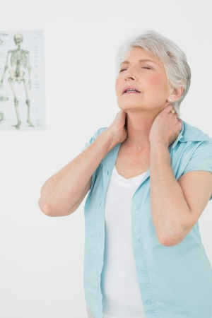 Senior woman suffering from neck pain with eyes closed in the medical officeの写真素材