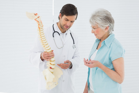 Male doctor explaining the spine to a senior patient in medical officeの写真素材