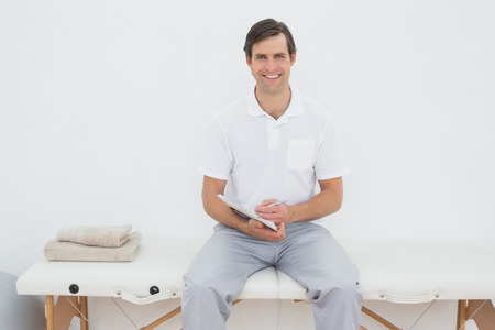 Portrait of a smiling male trainer with clipboard in the gym at hospitalの写真素材