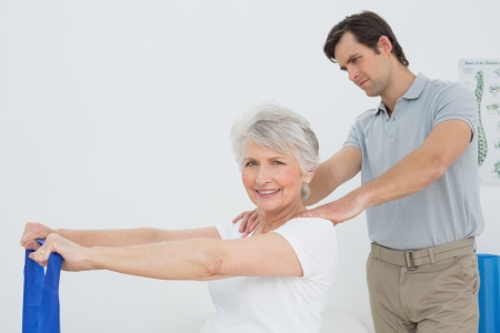 Male therapist assisting senior woman with exercises in the medical officeの写真素材