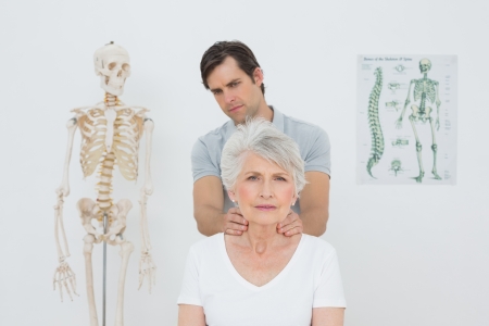 Male physiotherapist massaging a senior woman's neck in the medical officeの写真素材