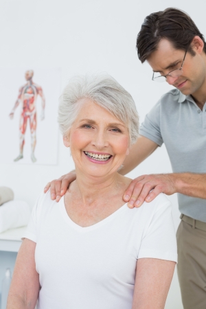 Male physiotherapist massaging a senior woman's shoulders in the medical officeの写真素材