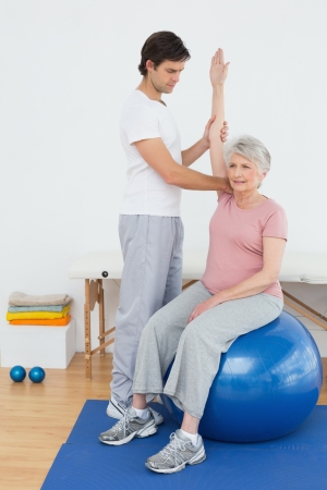 Senior woman sitting on yoga ball while working with a physical therapistの写真素材