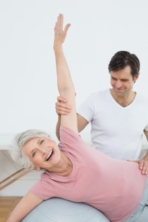 Physical therapist assisting senior woman with yoga ball in the gym at hospitalの写真素材