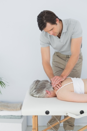 Male physiotherapist massaging a senior woman's back in the medical officeの写真素材