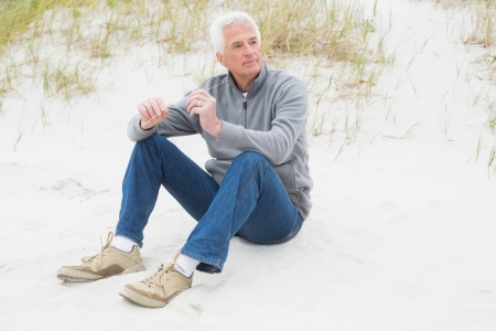 Full length of a casual senior man relaxing on sand at the beachの写真素材