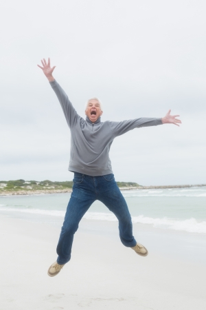 Full length portrait of a casual senior man jumping at the beachの写真素材