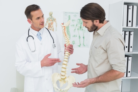 Male doctor explaining the spine to a patient in medical officeの写真素材