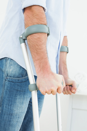 Close-up mid section of a young man with crutches standing in the medical officeの写真素材