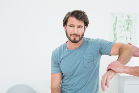 Male physiotherapist examining a young man's arm in the medical officeの写真素材