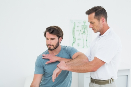 Male physiotherapist stretching a young man's hand in the medical officeの写真素材