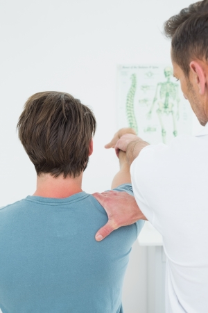 Rear view of a male physiotherapist stretching a young man's arm in the medical officeの写真素材