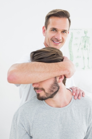 Portrait of a male chiropractor doing neck adjustment in the medical officeの写真素材