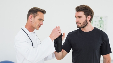 Male physiotherapist examining a young man's wrist in the medical officeの写真素材