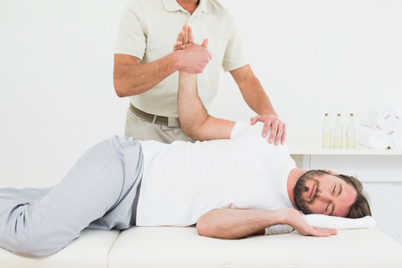 Male physiotherapist examining a young man's hand in the medical officeの写真素材