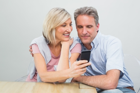 Happy casual couple looking at mobile phone in the houseの写真素材