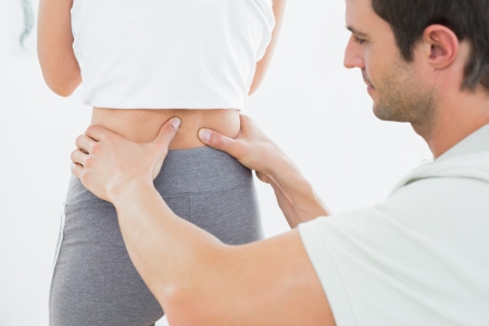 Close-up mid section of a physiotherapist examining woman's back in the medical officeの写真素材