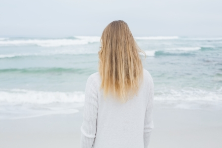 Rear view of a casual young blond standing at the beachの写真素材