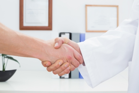 Close-up mid section of a doctor and patient shaking hands in the medical officeの写真素材