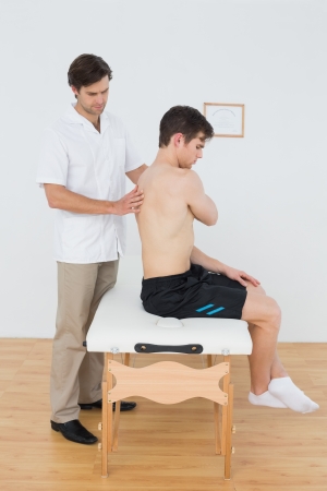 Side view of a shirtless man being examined by a physiotherapist in the medical officeの写真素材