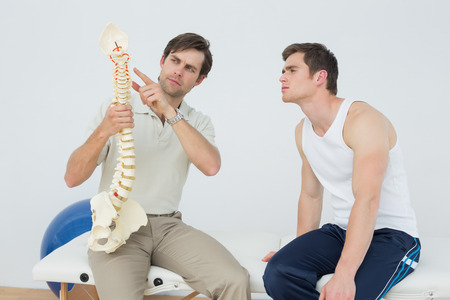 Male physiotherapist showing patient something on skeleton model in medical officeの写真素材