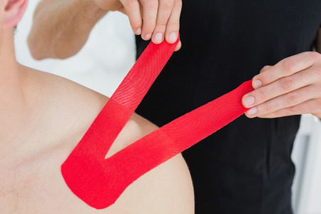 Close-up of a physiotherapist putting on red kinesio tape on patients shoulder in the medical officeの写真素材