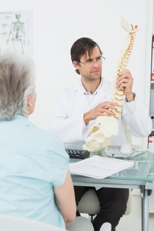 Male doctor explaining the spine to a senior patient in medical officeの写真素材