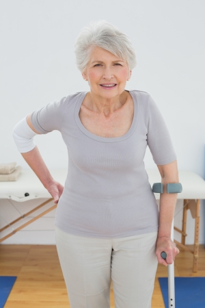 Portrait of a senior woman with crutch standing in the hospital gymの写真素材