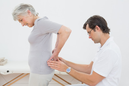 Side view of a male physiotherapist examining senior woman's back in the medical officeの写真素材