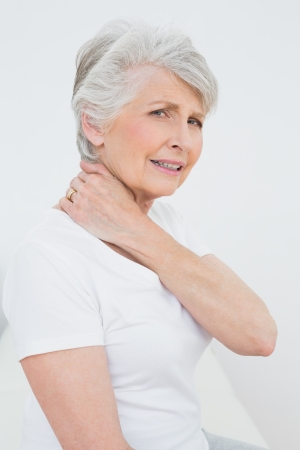 Side view portrait of a senior woman suffering from neck pain over white backgroundの写真素材