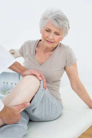Displeased senior woman getting her leg examined at the medical officeの写真素材