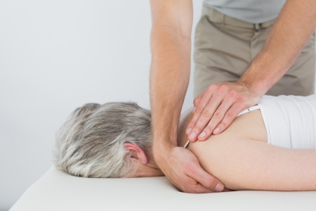 Male physiotherapist massaging a senior woman's shoulder in the medical officeの写真素材