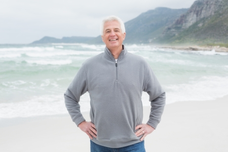Portrait of a happy handsome casual senior man with hands on hips at the beachの写真素材