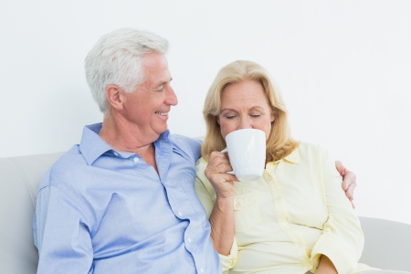 Relaxed senior couple with coffee cup sitting on sofa in a houseの写真素材