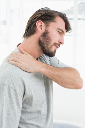 Side view of a young man suffering from shoulder pain in the medical officeの写真素材