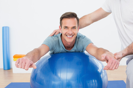 Physical therapist assisting young man with yoga ball in the gym at hospitalの写真素材