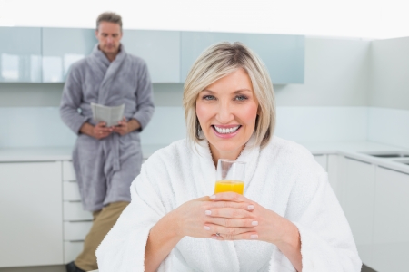 Woman with orange juice while man reading newspaper in background at the kitchenの写真素材