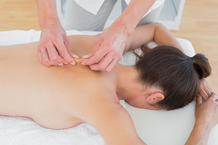 Close-up of a male physiotherapist massaging woman's back in the medical officeの写真素材