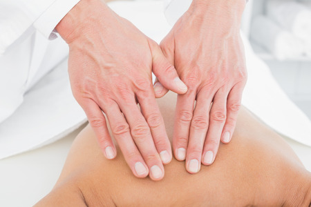 Close-up of a male physiotherapist massaging woman's back in the medical officeの写真素材