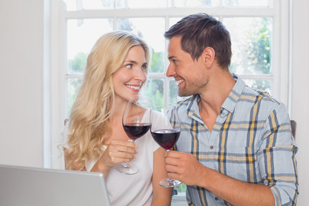 Happy loving young couple with wine glasses looking at each other at home