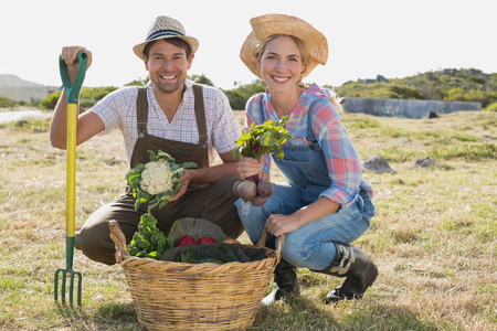 Full length portrait of a smiling young couple with vegetables in the fieldの写真素材