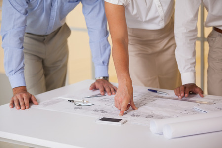 Close-up mid section of business people working on blueprints in the officeの写真素材