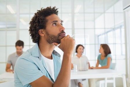 Close-up of a serious businessman with colleagues in meeting in background at the office