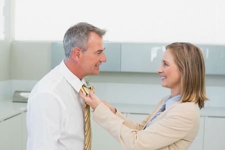 Side view of a woman adjusting businessman's tie in the kitchen at homeの写真素材