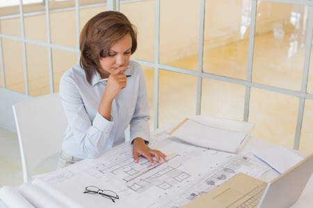 Concentrated young businesswoman working on blueprints in the office