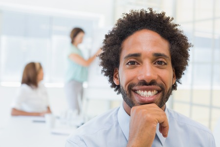Portrait of a smiling businessman with colleagues in meeting in background at the officeの写真素材