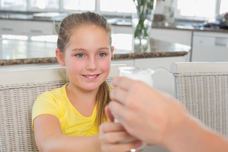 Little girl receiving glass of milk from mother in kitchen at homeの写真素材