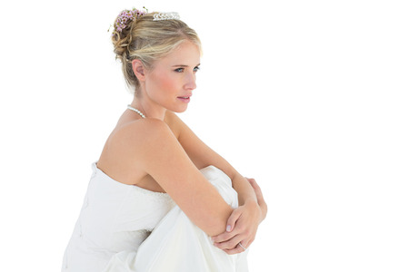 Side view of thoughtful bride hugging knees over white backgroundの写真素材