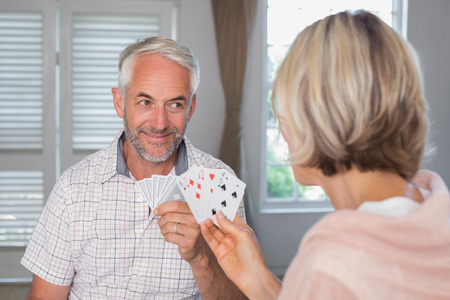 Close-up of a smiling mature man playing cards with woman at homeの写真素材